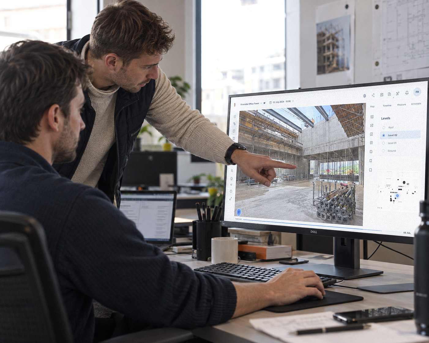 Zwei Kollegen zeigen am Computer auf einen 3D-Scan einer Baustelle.